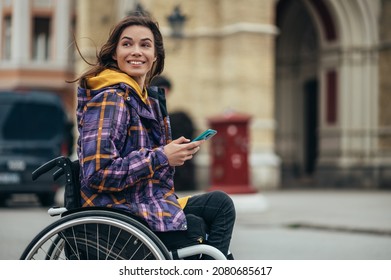 Joven hermosa mujer con discapacidad que usa una silla de ruedas usando un smartphone mientras estaba en la ciudad