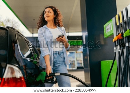 A young beautiful woman does not follow the safety rules and uses the phone while filling her car gas tank