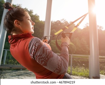 Young beautiful woman doing fitness training with suspension straps. Classes in the morning the park.