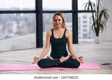 Young Beautiful Woman Doing Yoga In A Modern Bright Room With Large Windows. Yoga At Home Concept