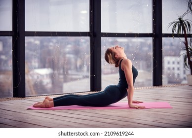 Young Beautiful Woman Doing Yoga In A Modern Bright Room With Large Windows. Yoga At Home Concept