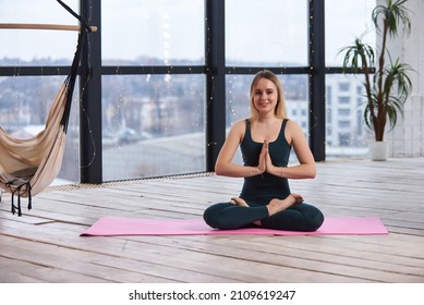 Young Beautiful Woman Doing Yoga In A Modern Bright Room With Large Windows. Yoga At Home Concept