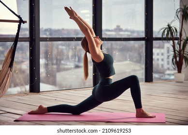 Young Beautiful Woman Doing Yoga In A Modern Bright Room With Large Windows. Yoga At Home Concept