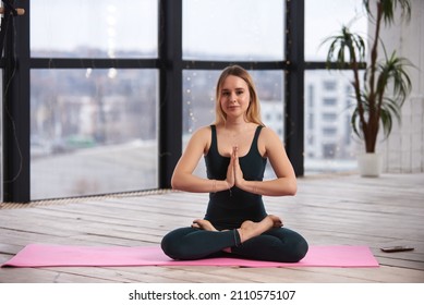 Young Beautiful Woman Doing Yoga In A Modern Bright Room With Large Windows. Yoga At Home Concept