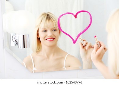 Young beautiful woman drawing big heart on mirror in bathroom.