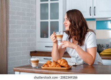 Young Beautiful Woman Drinking Coffee Cappuccino With Croissants In Kitchen At Cozy Home Interior. Smiling Caucasian 30s Woman Have Breakfast At Table During Morning Routine. Copy Space