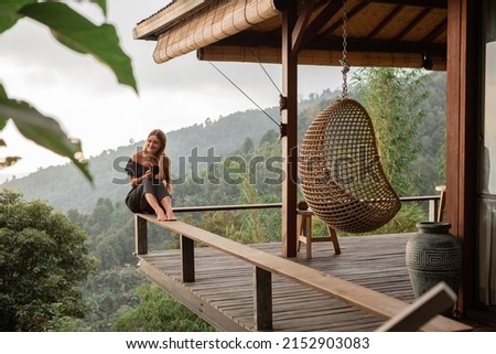 Young beautiful woman drinking coffee while sitting on a balcony in a wooden house overlooking the mountains