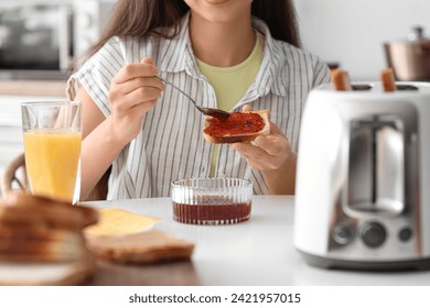 Young beautiful woman drinking orange juice and eating tasty toast with jam in kitchen, closeup - Powered by Shutterstock