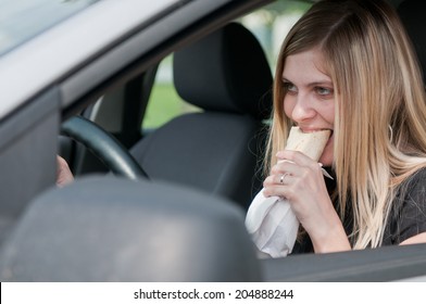 Young Beautiful Woman Driving Car And Eating Fast Food - Portrait Through Side Window