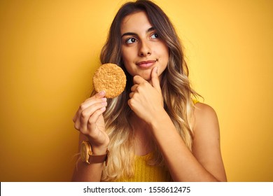 Young beautiful woman eating biscuit over grey isolated background serious face thinking about question, very confused idea