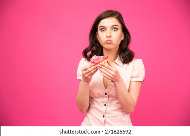 Young beautiful woman eating donut over pink background and looking at camera. Wearing in shirt