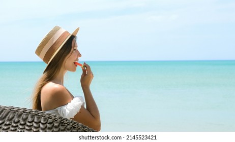 Young Beautiful Woman Eating Watermelon Slice, Stunning Turquoise Sea On Background. Romantic Girl In Straw Hat Relaxing In Outdoors Restaurant At Luxury Tropical Resort. Summer Vacations Concept.
