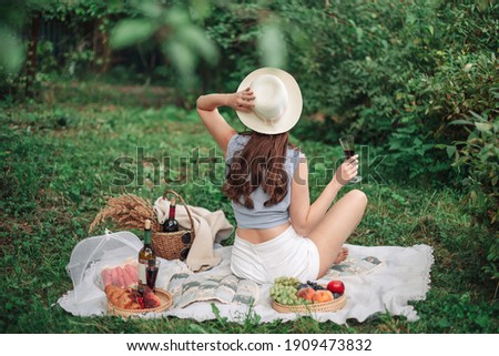Young beautiful woman enjoying ealthy picnic for a summer vacation with freshly baked croissants, fresh fruit and fruit salad, sandwiches and a glass of red vine laid out on white cloth