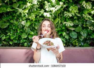 Young and beautiful woman enjoying heathy salad sitting at the vegetarian restaurant with living wall of green plants indoors. Healthy food concept