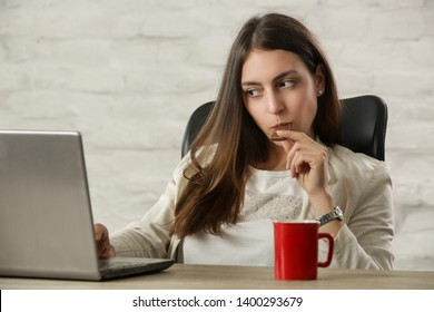 Young beautiful woman enjoying a piece of chocolate at the office table during a coffee break