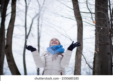 Young beautiful woman enjoying the snow falls outdoors in the forest.