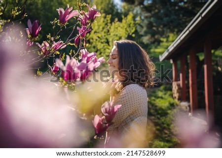 Young beautiful woman enjoying the spring of her home in the garden near a blooming magnolia tree inhaling the aroma