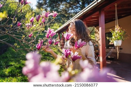 Young beautiful woman enjoying the spring of her home in the garden near a blooming magnolia tree inhaling the aroma