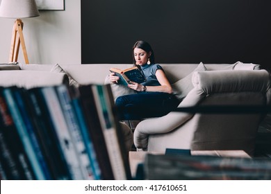 Young beautiful woman enjoys reading sitting on a comfortable couch. Learning and knowledge concept.