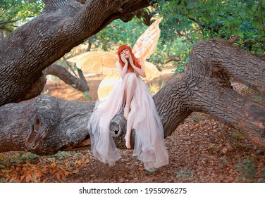 Young Beautiful Woman Fantasy Elf Sits On Branch Of Tree In Spring Forest. Green Trees Summer Park. Pixie Fairy Girl. Pink Silk Dress Gold Shiny Glowing Butterfly Wings. Costume Magic Creation Angel.