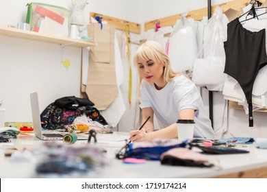 Young beautiful woman fashion designer working in atelier. Workspace of a creative fashion designer with a laptop, coffee, scissors, threads, fabrics and other elements