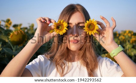 Young beautiful woman funny posing with sunflower flowers on hot summer day.