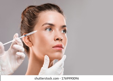 Young beautiful woman getting botox injection for eyes area over grey studio background, closeup, copy space