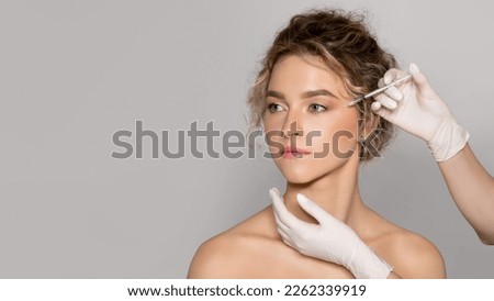 Young beautiful woman getting botox injection for eyes area, standing over grey studio background, panorama with copy space, banner