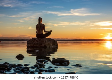 young beautiful woman girl are doing sport fitness yoga position on a stone at a beautiful lake, sea, see in the water - in the background you can see a colorful sundown - stone, water, orange sundown