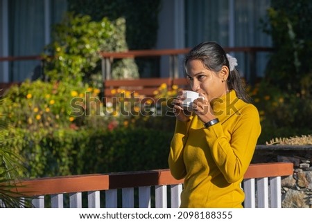 Young beautiful woman girl enjoying tea or coffee in a cup on a cold winter morning at a hill station on vacation, trip, workcation, in garden, park. Sweater, relaxing, entrepreneur, business, job.