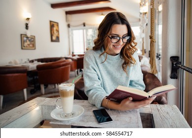 Young  beautiful woman in glasses reading interesting book in cafe   - Powered by Shutterstock