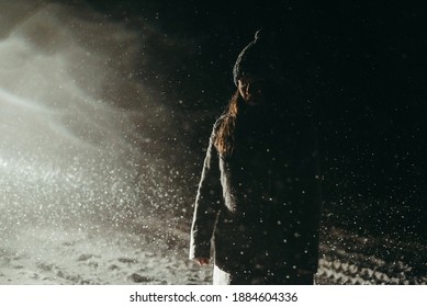 Young beautiful woman in a gray coat and hat stands in the snow at night on a dark background during a snowfall. Winter's tale, sad, cold, blizzard, snow. Emotional girl. Christmas mood, holiday