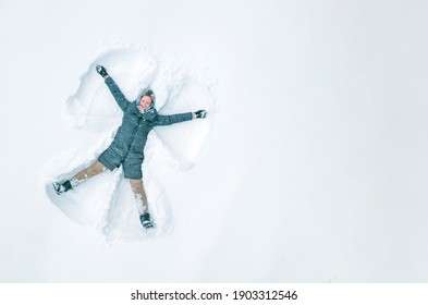 Young beautiful woman in a gray jacket, light pants, boots makes a snow angel in the snow, a view from a drone. Copy space, banner. Snow fun, entertainment.