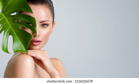 Young beautiful woman with green leave near face and body. Skin care beauty treatments concept.  Closeup girl's face with green leave. White model with clean, health skin of face - posing at studio