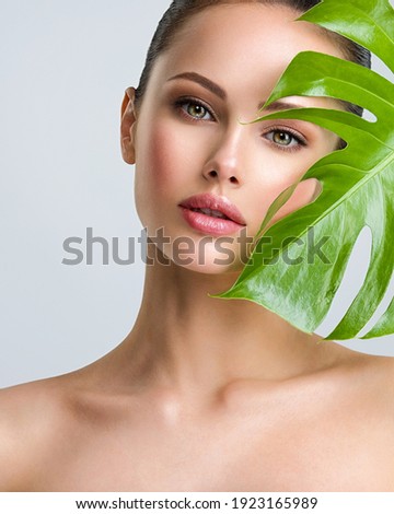 Young beautiful woman with green leave near face and body. Skin care beauty treatments concept.  Closeup girl's face with green leave. White model with clean, health skin of face - posing at studio