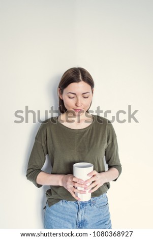 Young beautiful woman in green t-shirt and blue jeans stays on a white background with cup of tea