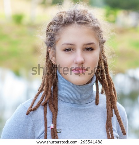 Young beautiful woman with hairdress dreadlocks close up against green grass.
