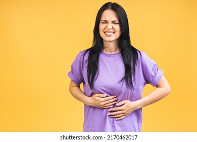 Young beautiful woman having abdominal pain isolated on yellow background.