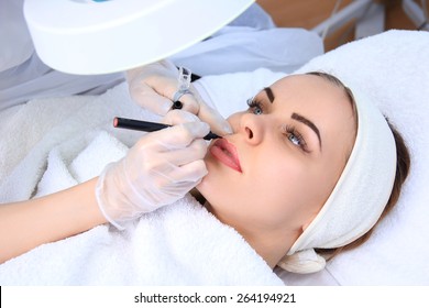 Young beautiful woman having permanent make-up (Tattoo)