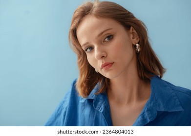 Young beautiful woman with healthy flawless radiant freckled skin wearing silver hoop earrings, linen shirt, posing on blue background. Close up studio beauty portrait. Copy, empty space for text - Shutterstock ID 2364804013