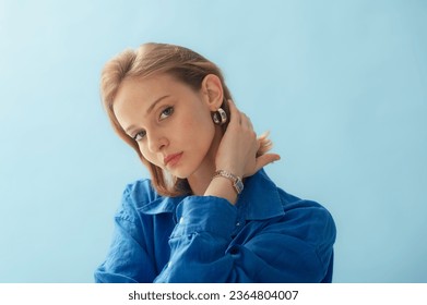 Young beautiful woman with healthy freckled skin wearing silver hoop earrings, wrist watch, linen shirt, posing on blue background. Close up studio  portrait. Copy, empty space for text - Shutterstock ID 2364804007
