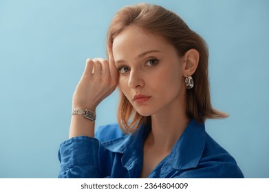 Young beautiful woman with healthy freckled skin wearing silver hoop earrings, wrist watch, linen shirt, posing on blue background. Close up studio  portrait. Copy, empty space for text - Shutterstock ID 2364804009