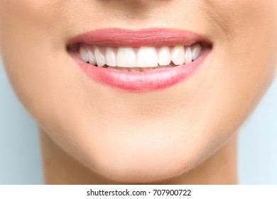 Young beautiful woman with healthy teeth smiling on light background, close up