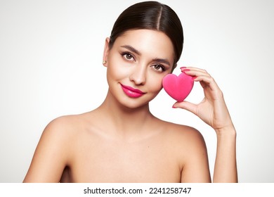 Young beautiful woman with heart-shaped gift. Girl with pure perfect face skin. Cosmetology, beauty and spa. Red nails manicure. Valentine’s Day