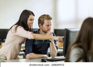 Young Beautiful Woman Helping Classmate Understand By Pointing At The Computer Screen