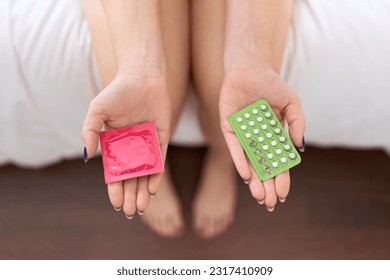 Young beautiful woman holding birth control pills and condom at bedroom