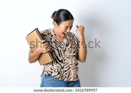 Young beautiful woman holding books very happy and excited doing winner gesture with arms raised, smiling and screaming for success. Celebration concept.