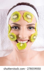 Young Beautiful Woman Holding Kiwi Fruit Slices On The Face In Spa Salon.