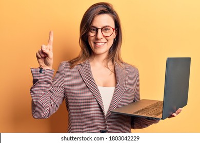 Young Beautiful Woman Holding Laptop Smiling With An Idea Or Question Pointing Finger With Happy Face, Number One 