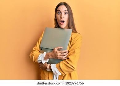 Young beautiful woman holding laptop afraid and shocked with surprise and amazed expression, fear and excited face. 